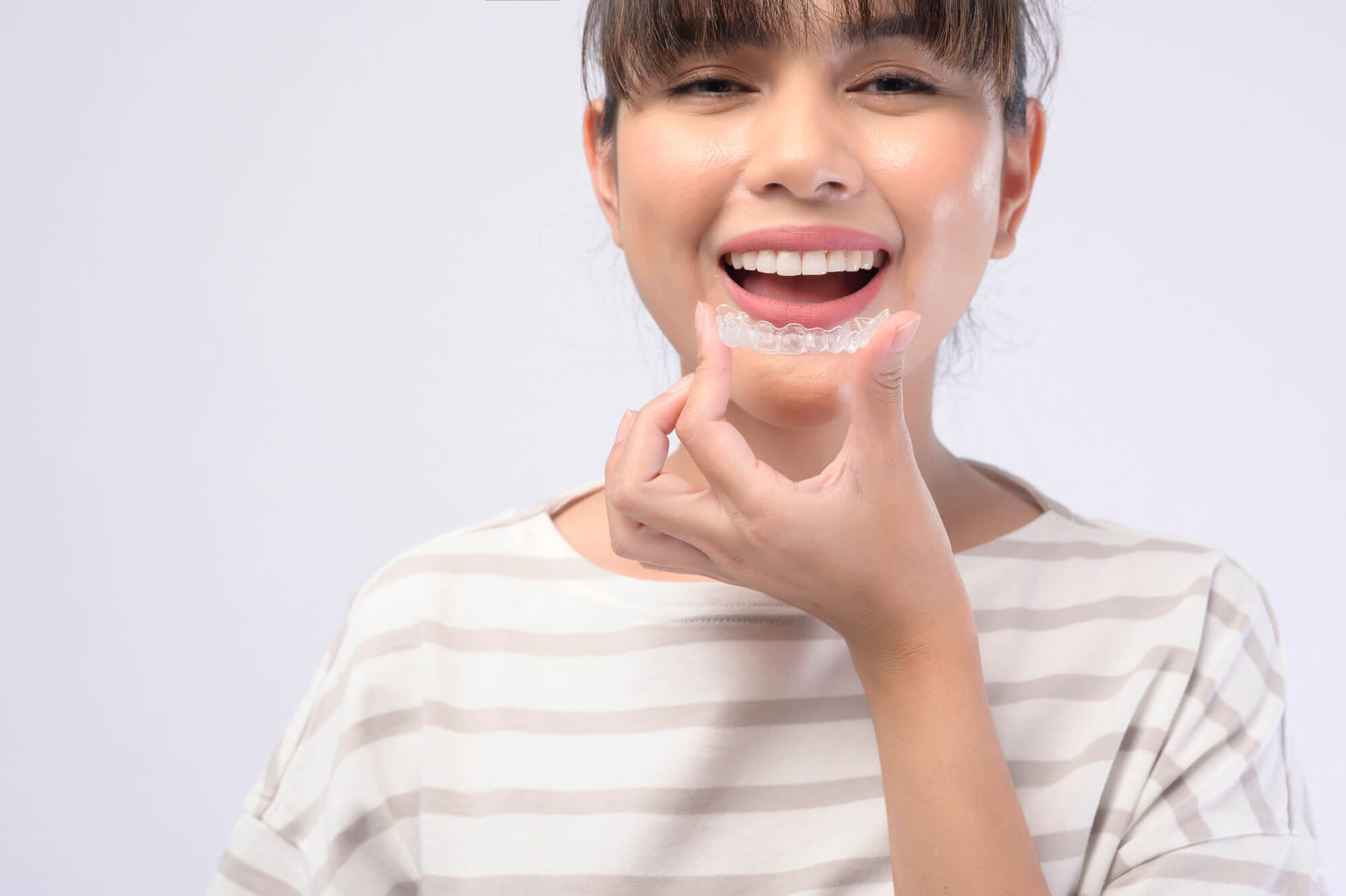 A young smiling woman holding invisalign braces over white background studio, dental healthcare and Orthodontic concept in Lisle, IL