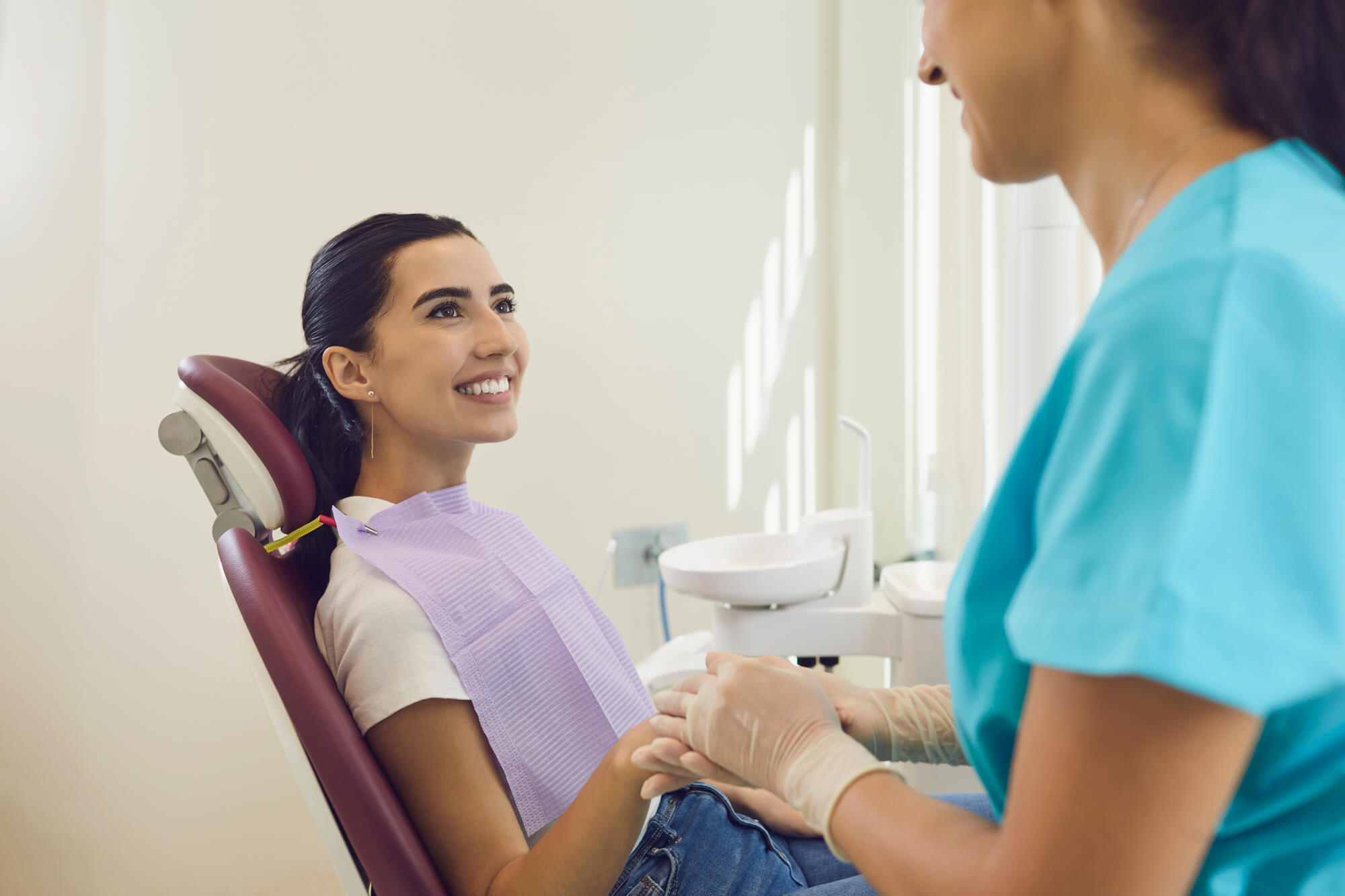 Happy, smiling patient sitting in chair at dental clinic office looking at dentist. Cropped hygienist holding hand of female client, reassuring her during check up, calming her down and building trust in Lisle, IL