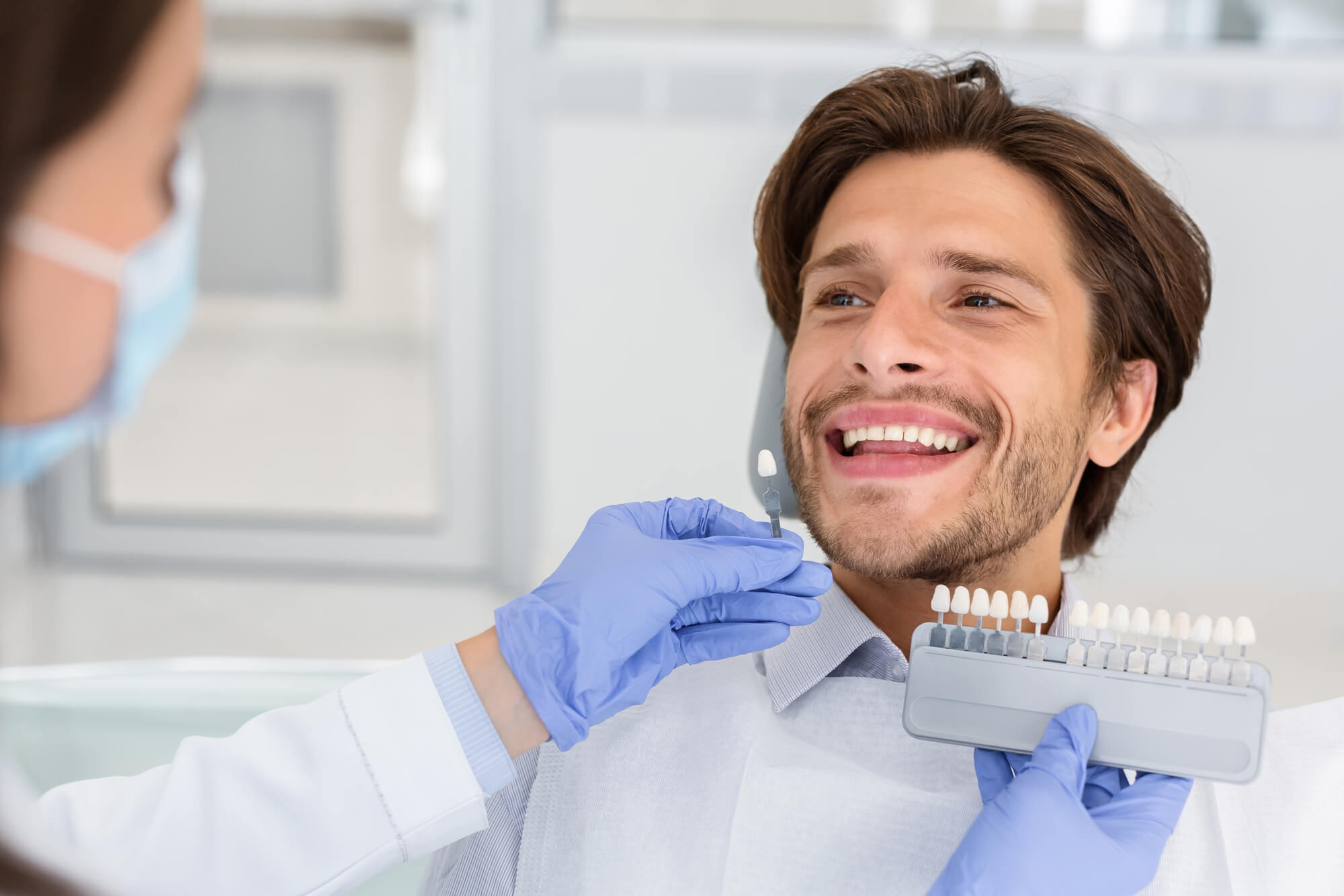 Dentist checking on male patient teeth color, using tooth enamel scale, dental office interior in Lisle, IL