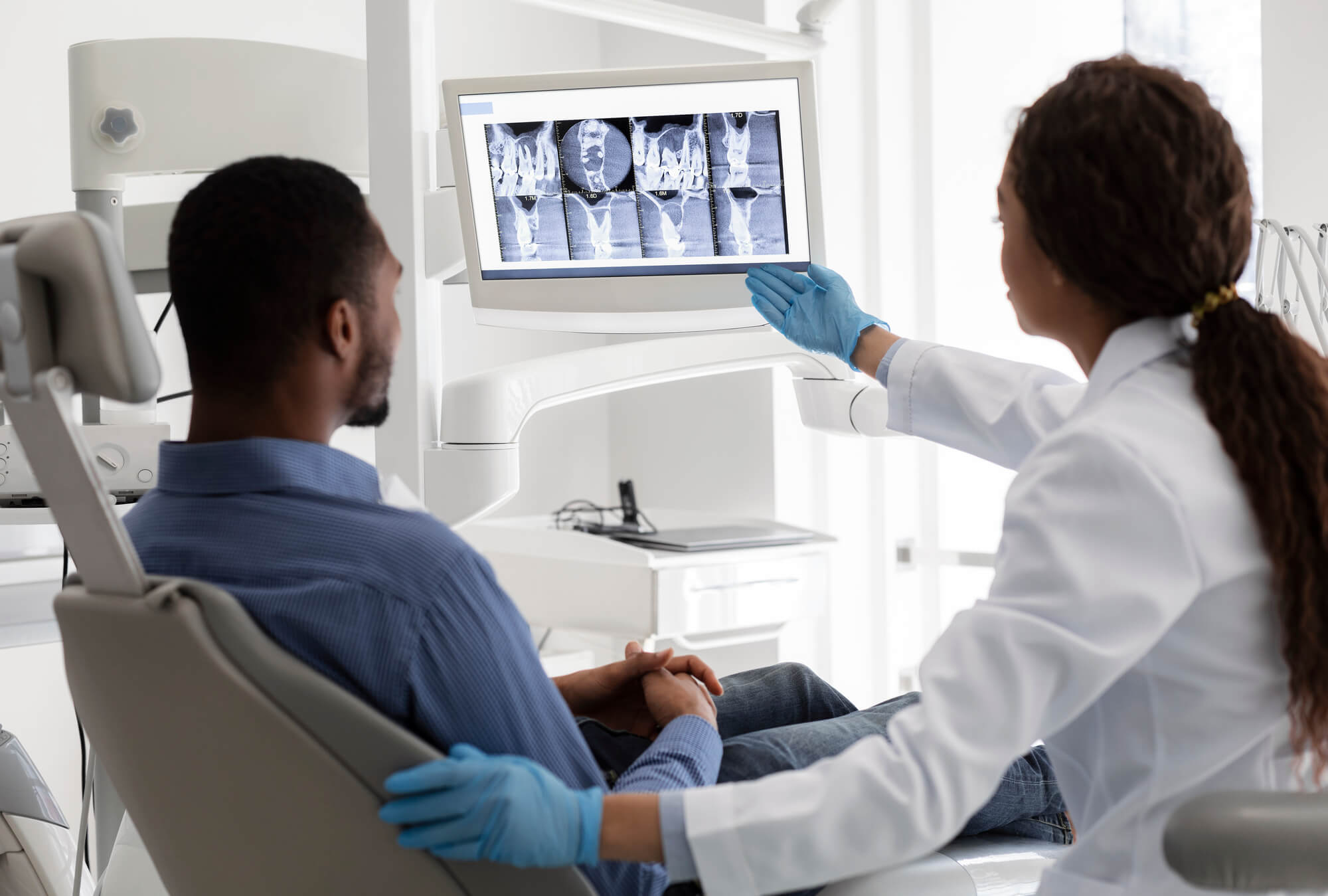 Female dentist african woman pointing at screen with xray picture, showing patient his teeth in Lisle, IL